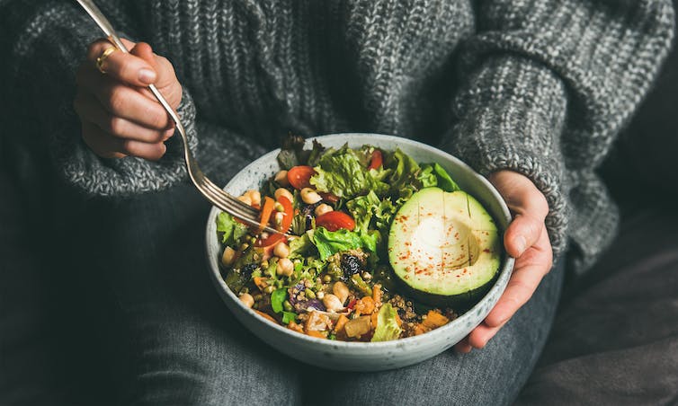 Kvinna som äter vegansk skål med sallad.